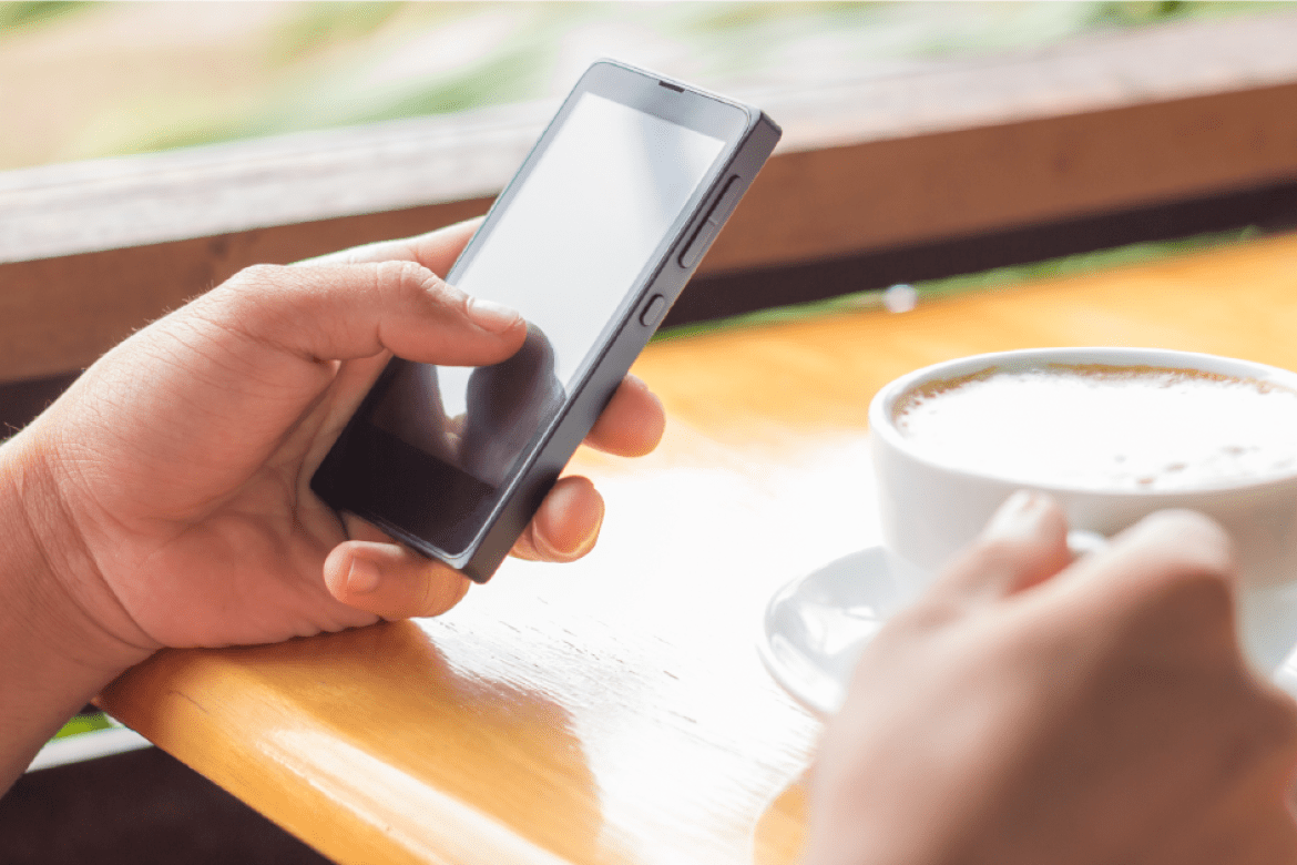 hands holding cell phone and coffee cup